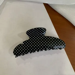 Close-up of large black hair claw clip with white polka dots for Y2K style