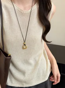 Detail van een Franse retro ketting met gouden hanger op een beige gebreide top.