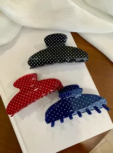Three polka dot hair claw clips in black, red, and navy blue on a minimalist white book