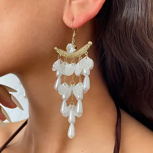 Close-up van elegante gouden halve maan oorbellen met witte bloemblaadjes en parels.