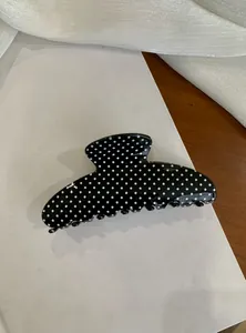 Close-up detail of a large black shark hair claw clip featuring classic white polka dots