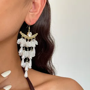 Detailopname van gouden oorbellen met witte bloemblaadjes en parels bij een model.