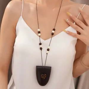 Detailaufnahme einer langen Perlenkette mit einem braunen Lederherz-Anhänger am Model.