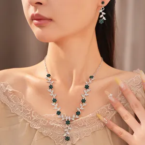 Vintage silver necklace and earrings set with green flower and leaf rhinestones on model.