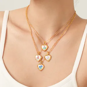 Détail de quatre pendentifs fleurs en émail en forme de cœur sur des colliers dorés.