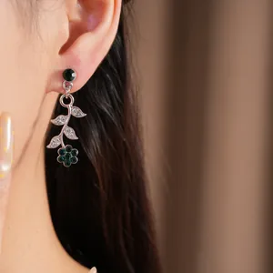 Close-up detail of silver-toned vine earring with dark green stones worn on model ear