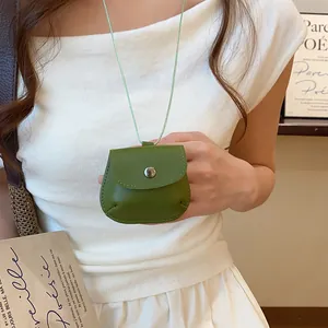 Close-up van een groene lederen tasjesketting gedragen op een wit geplooide top.