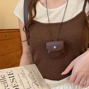 Detailopname van een vintage bruine leren tasjesketting op een bruine gebreide top.