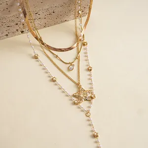 Primo piano di una collana d'oro a più strati con perle, stelle e ciondolo cuore zircone.