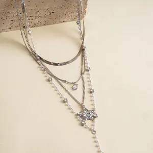 Dettaglio di una collana argentata a strati con stelle e perle su un supporto in pietra.