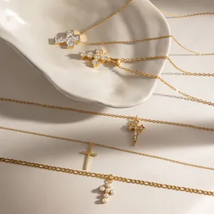 Primo piano di diverse collane a croce dorate con zirconi e perle su un vassoio di ceramica