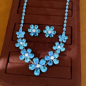 Elegantes Set aus Halskette und Ohrringen mit hellblauen Zirkon-Blumen auf braunem Samt