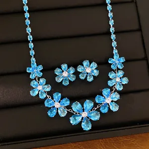 Close-up of blue zircon flower necklace and earrings set on a black jewelry display pad.