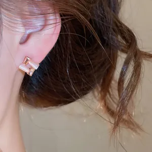 Detailed macro view of geometric cat-eye stone earrings in rose gold finish on model's ear