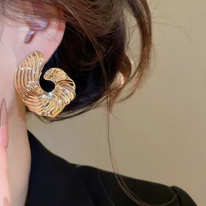 Nahaufnahme von goldenen Metallohrringen mit Falten-Design am Ohr