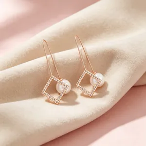 Detailaufnahme der roségoldenen quadratischen Ohrringe mit Strasssteinen und Muschelperlen.