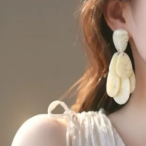Close-up of elegant cream marbled resin water drop tassel earrings on a model's ear