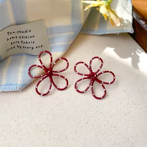 Detailed view of red hollowed-out flower earrings with white polka dots and silver needle