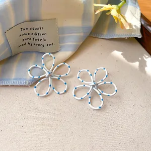 Detailed close-up of white hollow flower stud earrings with blue polka dot pattern