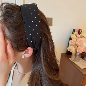 Nahaufnahme eines schwarzen Stoff-Stirnbandes mit weißen Kreuzen auf braunem Haar