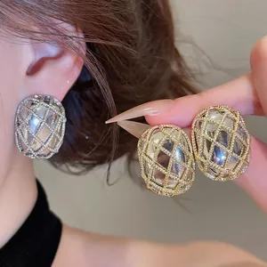 Primo piano di eleganti orecchini a griglia ovale in metallo oro e argento lucido.