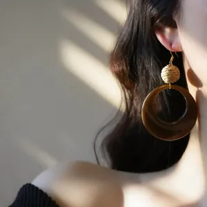 Vue détaillée de boucles d'oreilles ethniques en raphia et résine sur un mannequin au soleil