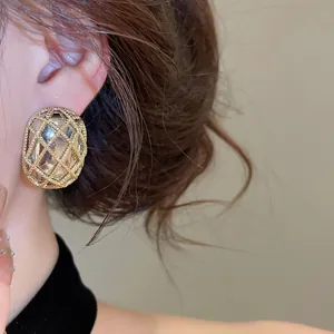 Dettaglio ravvicinato di un elegante orecchino a perno ovale a maglia dorata su una modella