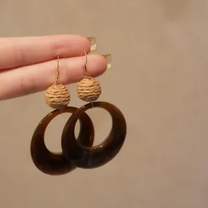 Détail en gros plan de boucles d'oreilles ethniques avec boules en raphia et résine brune
