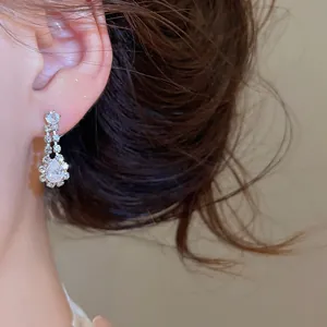 Nahaufnahme von eleganten Zirkonia-Ohrringen mit Wassertropfen an einem Model-Ohr