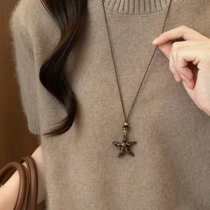 Detail van een vintage luipaardprint zeester hanger aan een bruine leren koordketting