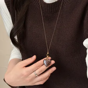 Close-up van een hartvormige hanger met luipaardprint aan een bruin leren koordketting