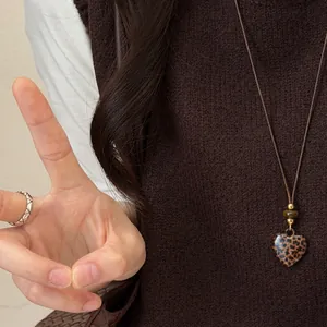 Detail van luipaardprint hart hanger aan een vintage bruine leren koordketting