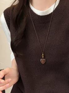 Detailopname van een ketting met luipaardhart-hanger en kralen op een bruin vest