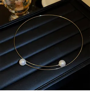Choker minimaliste en fil d'or avec deux perles sur support noir élégant.