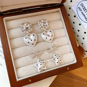 Vue détaillée de boucles d'oreilles argentées en forme de cœur et d'étoile dans un écrin.