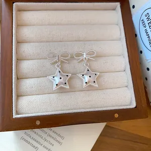 Gros plan de boucles d'oreilles nœud argenté avec pendentifs étoile à pois en boîte