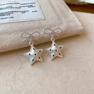 Vue détaillée de boucles d'oreilles nœud et étoile argentées avec motifs à pois noirs