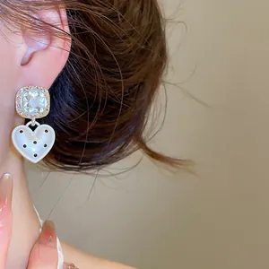 Gros plan d'une boucle d'oreille pendante en cœur à pois noirs sur une tige en argent massif.