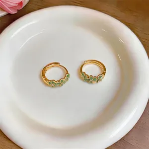 Detailopname van elegante gouden oorringen met delicate groene bloemmotieven op een bord
