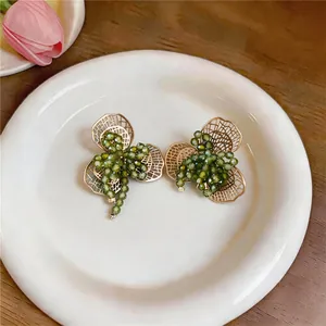 Close-up van groene kralen bloem oorbellen op een wit bord met gouden details.