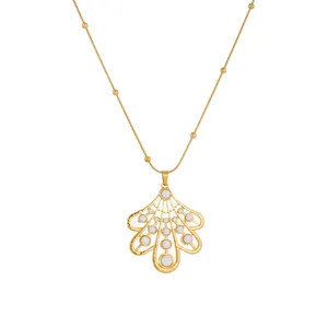 Détail d'un collier pendentif feuille doré baroque avec des inserts en émail blanc