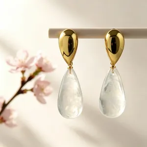 Detailaufnahme eleganter Tropfenohrringe mit goldenem Finish und weißer Harztextur für Damen