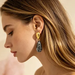 Nahaufnahme eines eleganten Goldohrrings mit einem grau marmorierten Harzanhänger