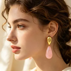 Elegante Nahaufnahme einer Frau mit goldenen Wassertropfenohrringen und rosa Harz