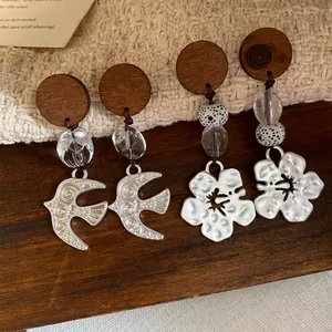 Detailopname van handgemaakte houten oorbellen met zwaluw- en bloemmotief en kralen