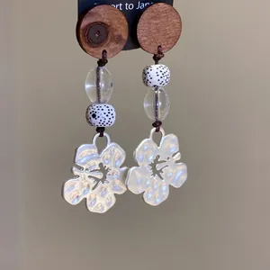 Detailweergave van oorbellen met houten cirkels, glasparels en zwaluwbloemhangers.