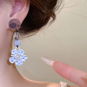 Detailopname van houten en glazen kraaloorbellen met een zwaluwbloem hanger in zilveren kleur