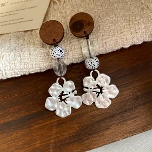 Detail van houten oorbellen met gespikkelde kralen en zilveren zwaluw bloem bedeltjes.