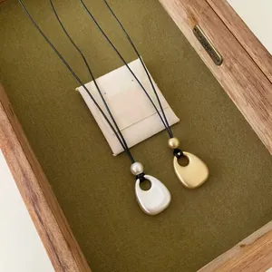 Gros plan de colliers avec pendentif goutte en métal mat doré et argenté sur cordon noir