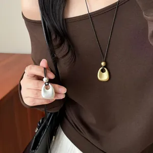 Vue détaillée de colliers à pendentifs en métal mat doré et argenté avec cordons noirs.